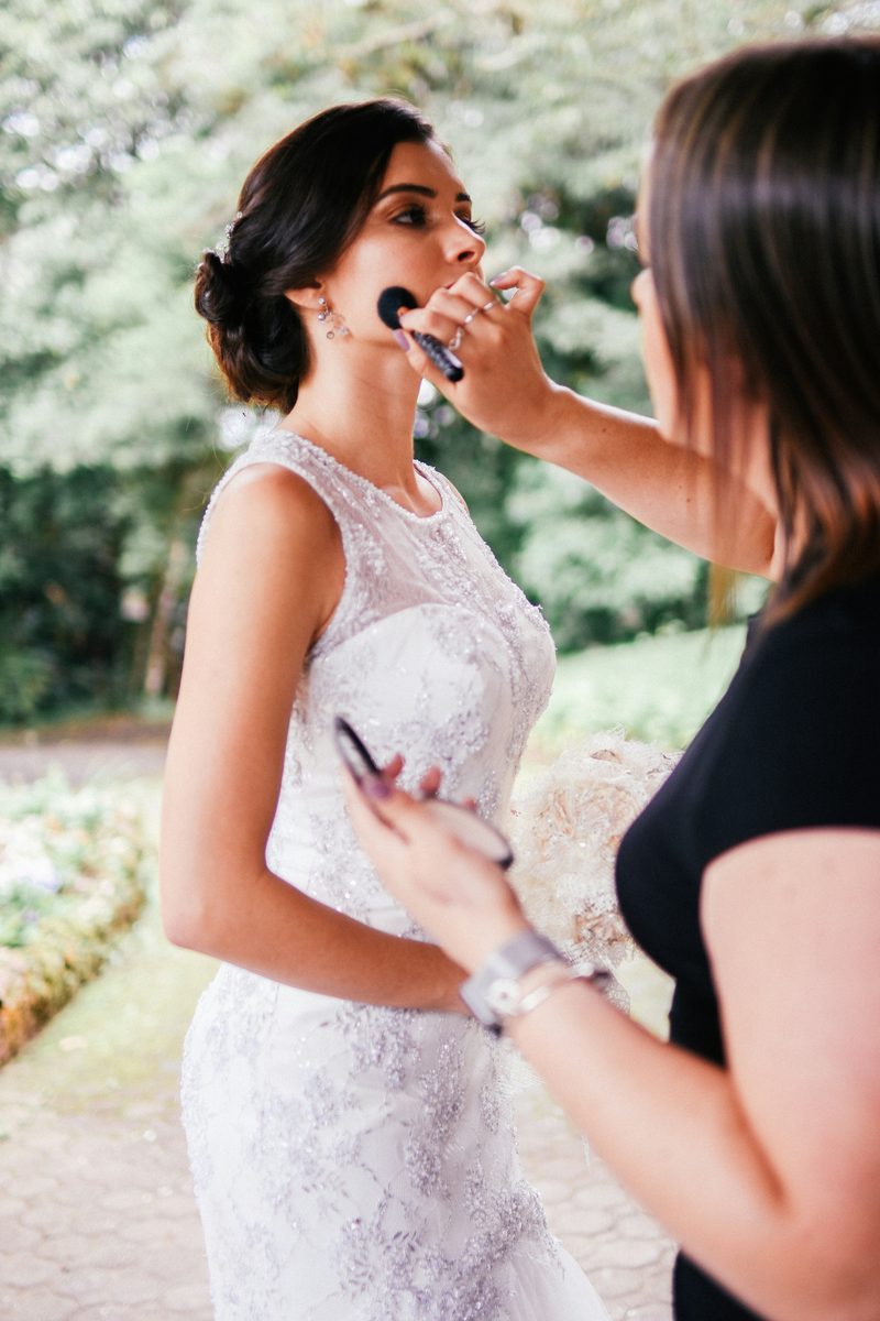 A makeup artist applying bridal makeup to a bride in her wedding dress